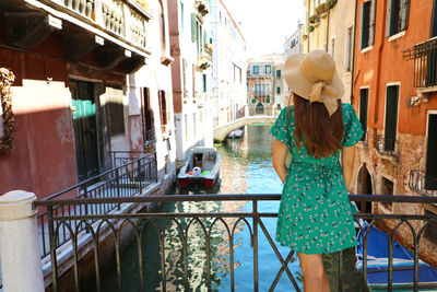 Rear view of woman standing over canal by railing in city