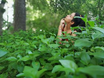 Thoughtful woman sitting amidst plants in forest