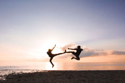 Silhouette men jumping at beach against sky during sunset