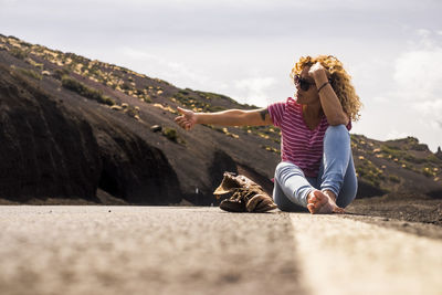Woman hitchhiking while sitting on road