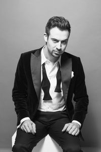 Portrait of young man in suit sitting against gray background