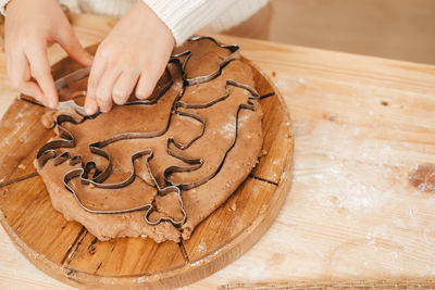Children's hands carve cookies on gingerbread dough from figurines.