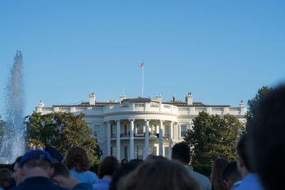 Rear view of people standing in front of white house