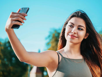 Young woman taking selfie through smart phone against sky