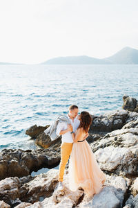 Couple on rock by sea against sky