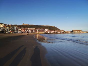 Scenic view of beach by buildings against clear blue sky