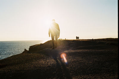 Rear view of silhouette man walking at beach against sky during sunset