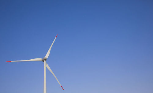 Low angle view of wind turbine against clear blue sky