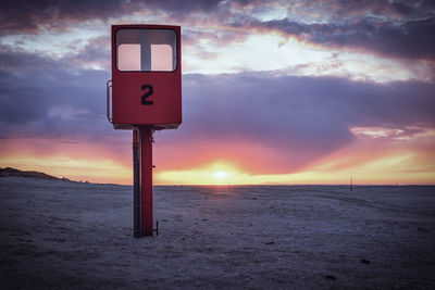 Information sign on beach against sky during sunset