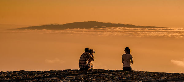 Rear view of couple standing against orange sky