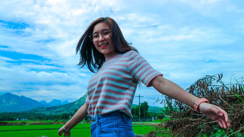 Portrait of smiling young woman standing on field against sky