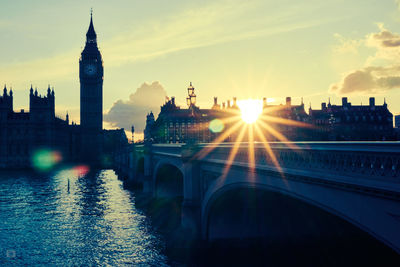 Westminster bridge over thames river by big ben against bright sky at morning