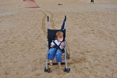 High angle view of boy sitting on baby stroller at beach