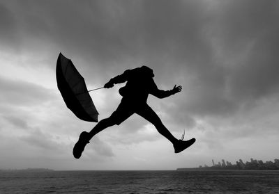 Silhouette man jumping in sea against sky