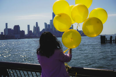 Rear view of woman standing in city holding yellow balloons