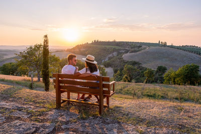 Rear view of couple sitting on bridge at sunset