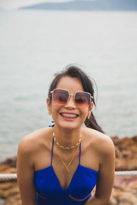 Smiling asian woman in a blue wear with braces on her teeth with sea and sky background.
