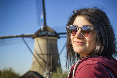 Portrait of young woman against windmill and clear sky