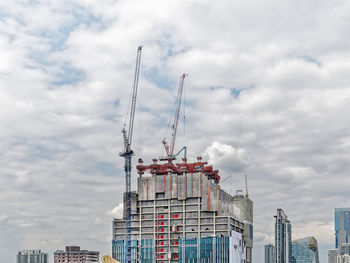 Under construction building with cranes against cloudy sky