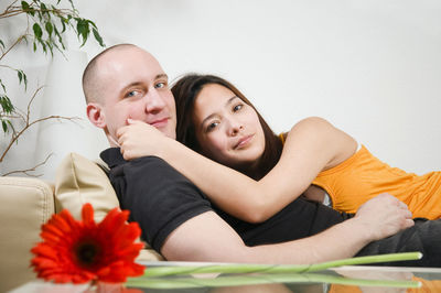 Double portrait of a young heterosexual couple hugging on a couch at home in front of a bright wall.