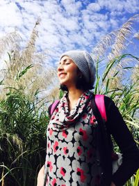 Low angle view of smiling woman by plants against sky