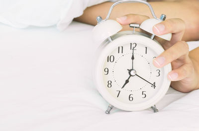 Close-up of woman holding alarm clock in bed