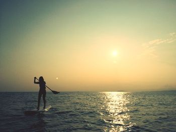 Silhouette woman paddleboarding on sea against sky during sunset