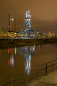 Illuminated built structure by river against sky at night