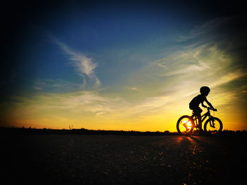 Silhouette person riding bicycle on field during sunset