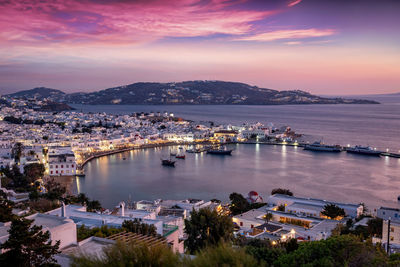 Illuminated cityscape by sea against sky during sunset