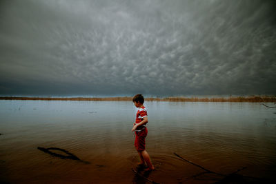 Boy standing in lake against sky