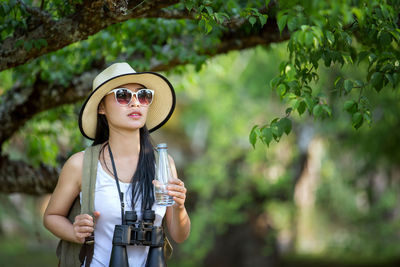 Young woman holding water bottle by tree