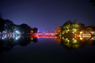 Illuminated city by lake against sky at night