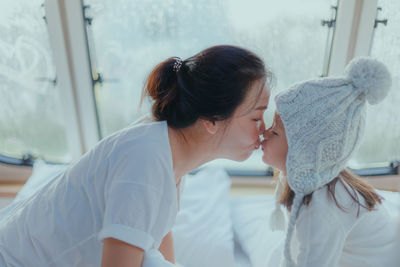 Mother kissing daughter on bed at home