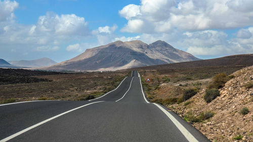 Empty road towards mountains against sky