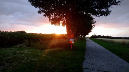 Road amidst field against sky during sunset