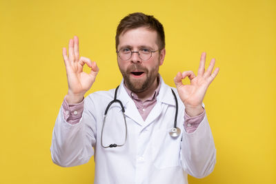 Midsection of man with arms raised standing against yellow background