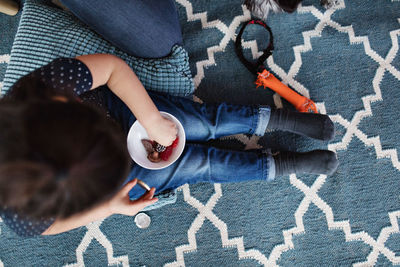 Directly above shot of girl eating candies while sitting on carpet at home