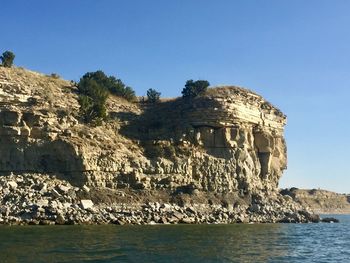 Rock formations by sea against clear blue sky