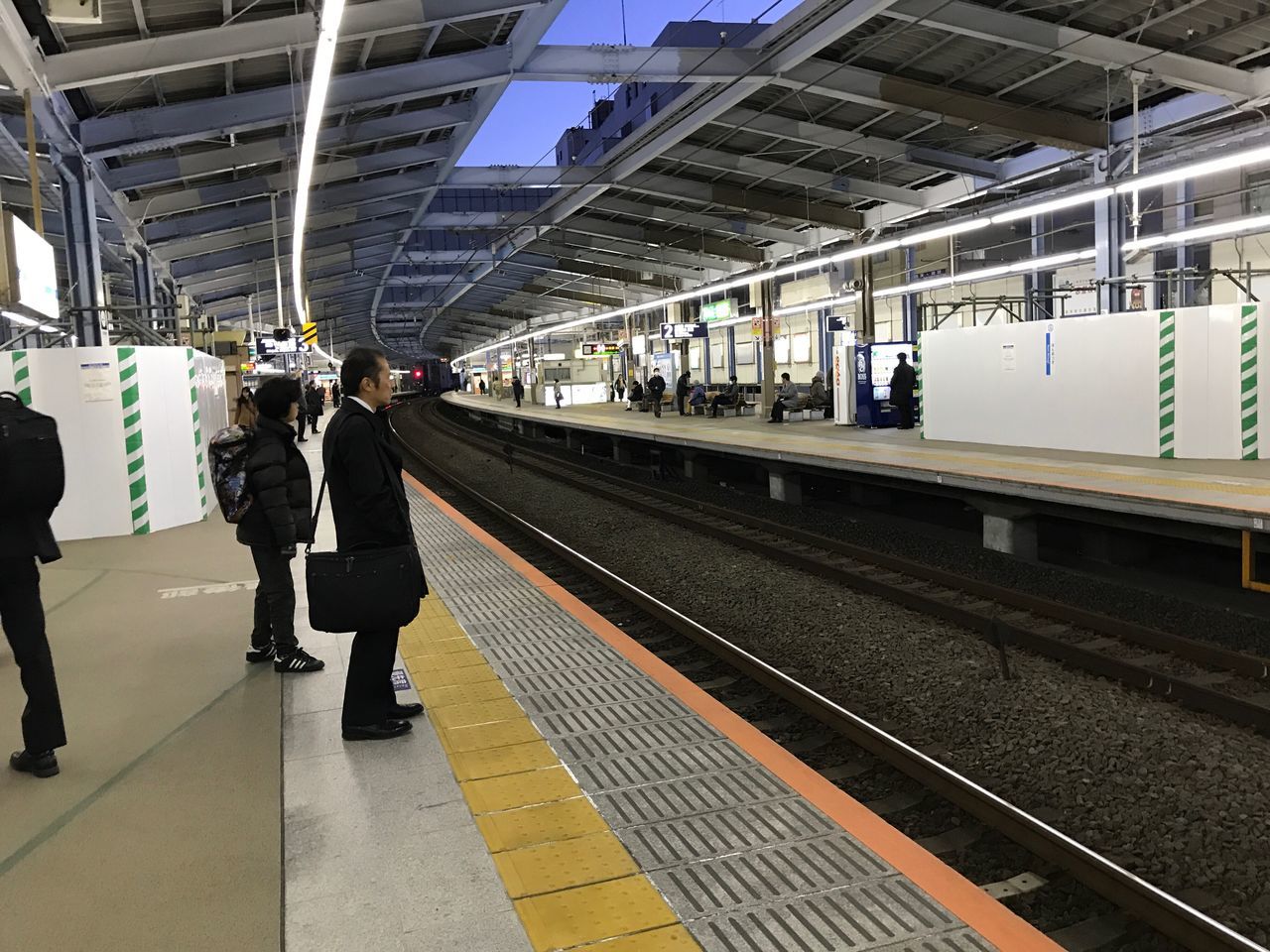 railroad station platform, transportation, real people, public transportation, railroad station, rail transportation, railroad track, men, full length, lifestyles, women, standing, indoors, rear view, train - vehicle, waiting, commuter, one person, day, adult, people