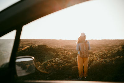 Female backpacker looking at horizon while standing on meadow during sunset