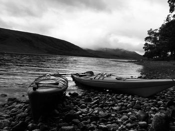 Boats moored on shore by lake against sky