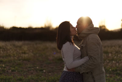 Couple kisses in a natural landscape at sunset.
