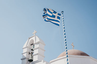 Low angle view of a greek flag on a traditional  whitewash building against clear blue sky