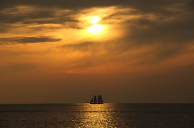 Silhouette of sailboat sailing in sea against dramatic sky