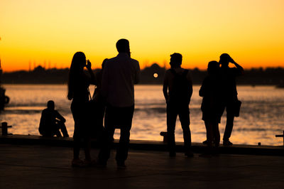 Friends on footpath by sea against sky during sunset