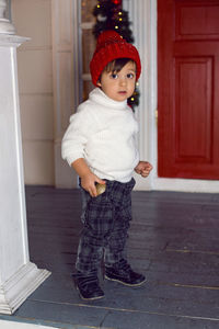 Boy stands on the porch of the house in a sweater and a red hat