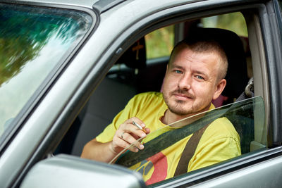 Portrait of man holding cigarette while sitting in car