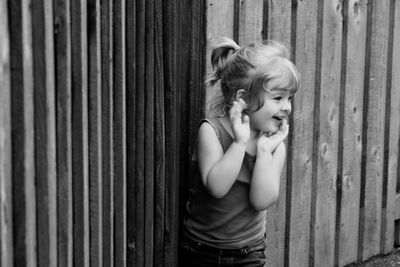 Cute girl with hand on cheek looking away while standing against fence