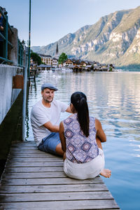 Rear view of friends sitting on lake against mountains